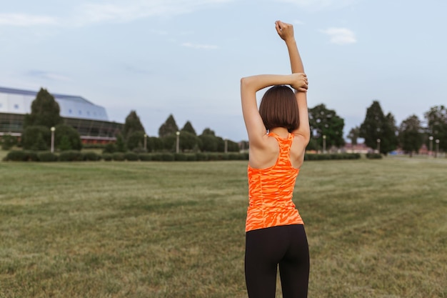 athletic runner in orange neon top stretching arms above head and warming up