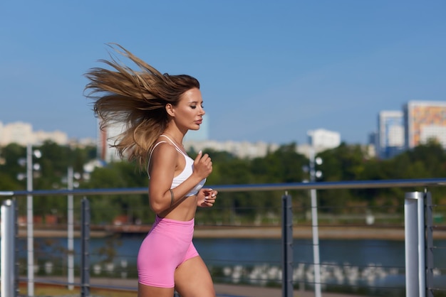 Athletic slim woman on a sunny day runs along the embankment or park