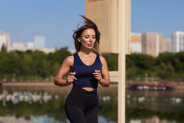 Athletic slim woman on a sunny day runs along the embankment or park