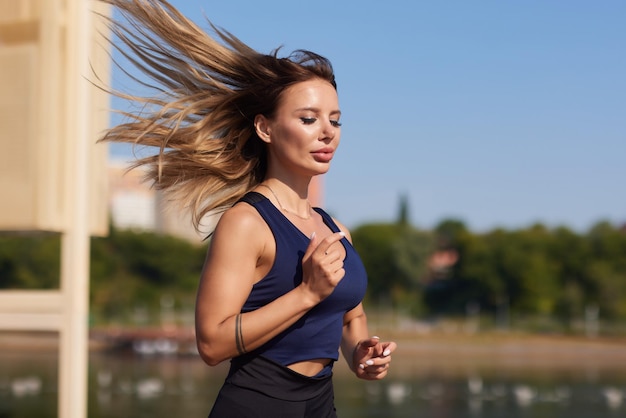 Athletic slim woman on a sunny day runs along the embankment or park