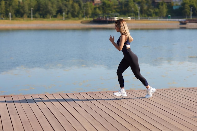 Athletic slim woman on a sunny day runs along the embankment or park