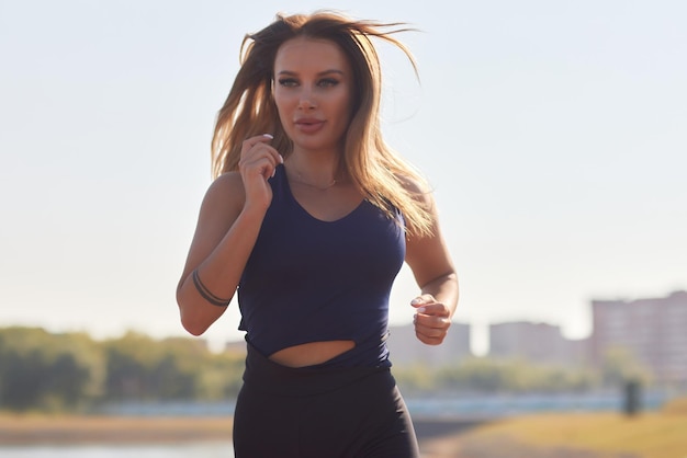 Athletic slim woman on a sunny day runs along the embankment or park