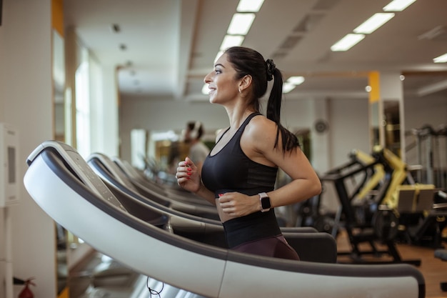 Athletic smiling woman running on treadmill doing cardio workout in gym