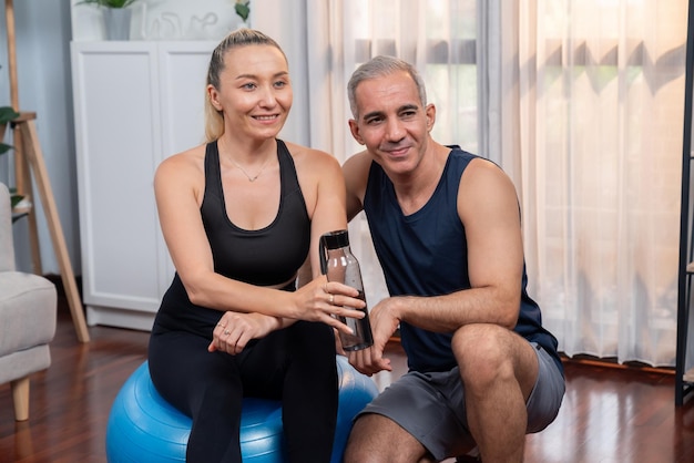 Athletic and sporty senior couple portrait in sportswear sitting on sofa with fitness water bottle as home exercise concept Healthy fit body lifestyle after retirement Clout