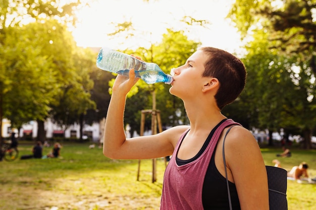 athletic teenage girl, in clothes, drinks water from a bottle after sports training, yoga