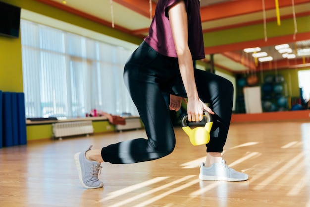 Athletic woman exercising with kettle bell while being in squat position. Muscular woman doing cross fit workout at gym.