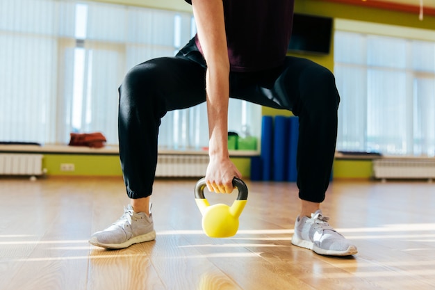 Athletic woman exercising with kettle bell while being in squat position. Muscular woman doing cross fit workout at gym.