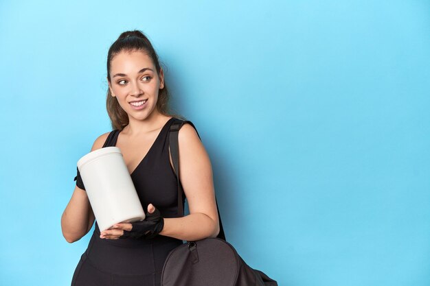 Athletic woman holding a protein bottle in a blue studio background