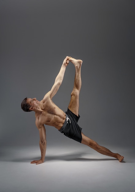 Athletic yoga doing stretching exercise in studio, grey wall Strong man practicing yogi , asana training, top concentration, healthy lifestyle