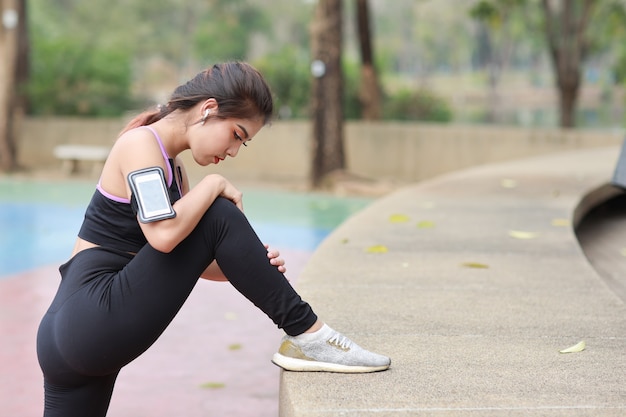 Athletic young healthy and beauty asian woman in sportswear standing and stretching outdoor for morning exercise. Active girl work out on biceps practice with mobile phone. Sport and lifestyle concept