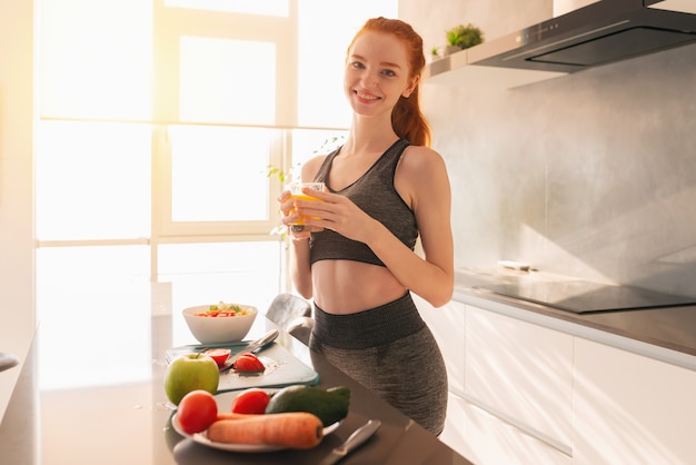 Athletic young red haired woman in the kitchen with a glass of fruit centrifuged juice