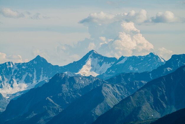 Atmospheric alpine landscape with giant low cloud above great glacier mountain with sunlight on snow. Big rocks and mountains under cloudy sky in sunny day. Awesome minimalist highland scenery.