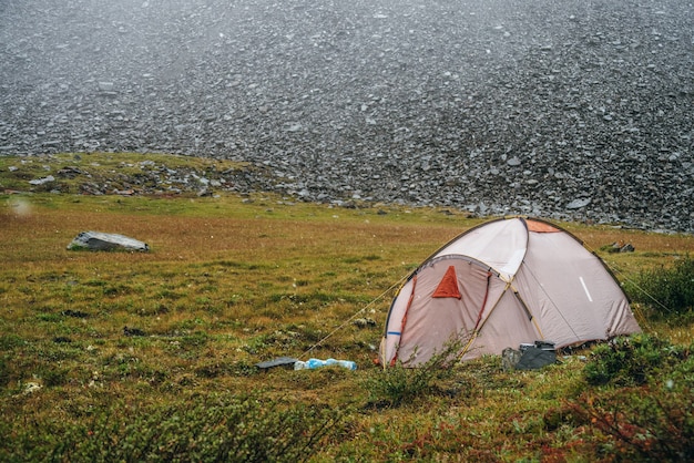 Atmospheric alpine scenery with tent in mountains during snowfall. Beautiful snowfall in high mountains. Scenic green mountain landscape with flakes of snow above tent. Large snowflakes in highlands.