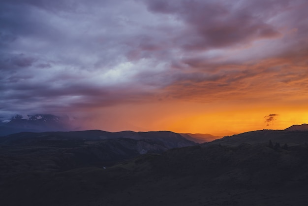 Atmospheric landscape with silhouettes of mountains with trees on background of vivid orange blue violet dawn sky. Colorful nature scenery with sunset or sunrise of illuminating color. Sundown paysage