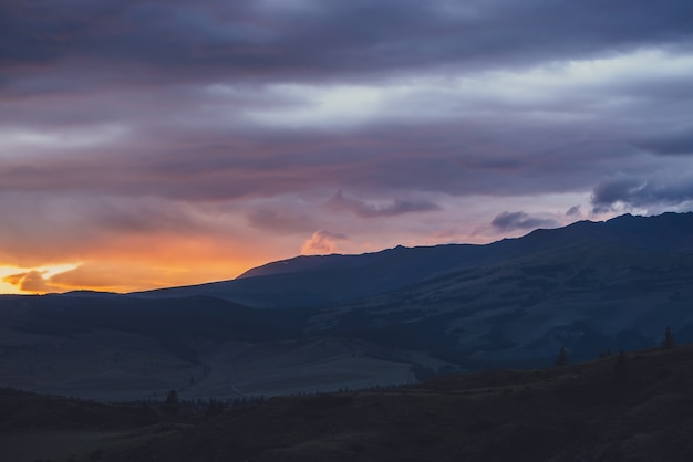 Atmospheric landscape with silhouettes of mountains with trees on background of vivid orange blue violet dawn sky. Colorful nature scenery with sunset or sunrise of illuminating color. Sundown paysage