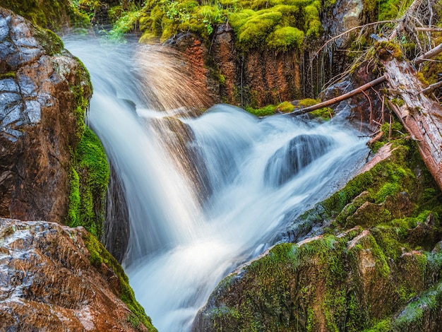 Atmospheric minimal landscape with a long exposure of a large waterfall on a green rock. Nature background of turbulent falling water stream on wet rocks.