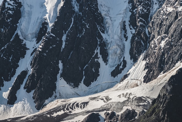 Atmospheric minimalist textured alpine landscape of snowy rocky mountain with glacier tongue. Background of snowbound mountainside. Cracks on ice on steep slope. Majestic scenery on high altitude.