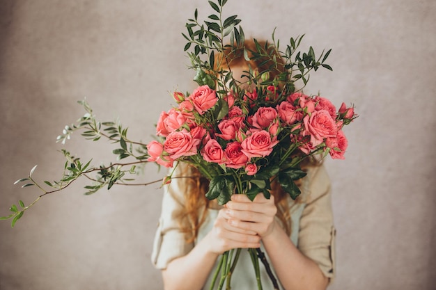 Atmospheric photo of a girl who covers her face with a bouquet of pink roses