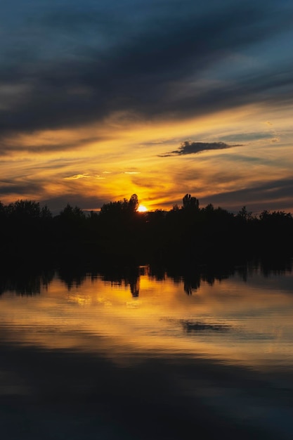 Atmospheric sunset behind trees and reflection in water