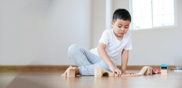 Attention asian boy playing wood block building rail way and road on the floor at home