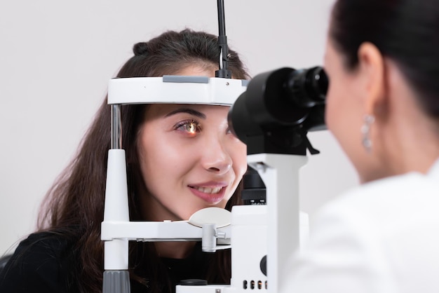 Attentive optometrist examining beautiful female patient with slit lamp in ophthalmology clinic Optometrist during an examination in a modern clinic Eyesight check Closeup of a female patient