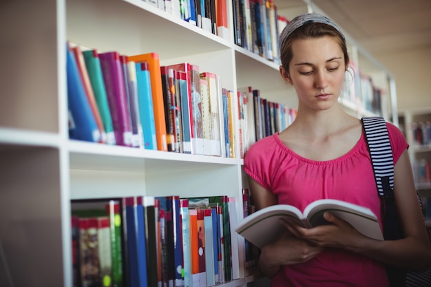 Attentive schoolgirl reading book in library