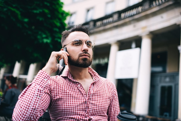 Attentive trendy male speaking on mobile on street