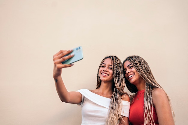 Attractive african american sisters with cool braids smiling and taking selfie in the street