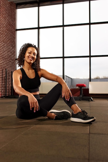 Attractive african american woman in sportswear looking at camera and smiling while sitting on the