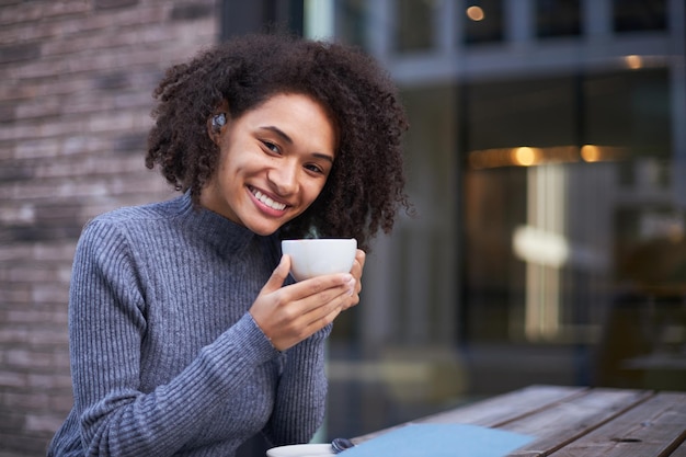 Attractive African American young woman holding a cup of aroma coffee and smiling at camera