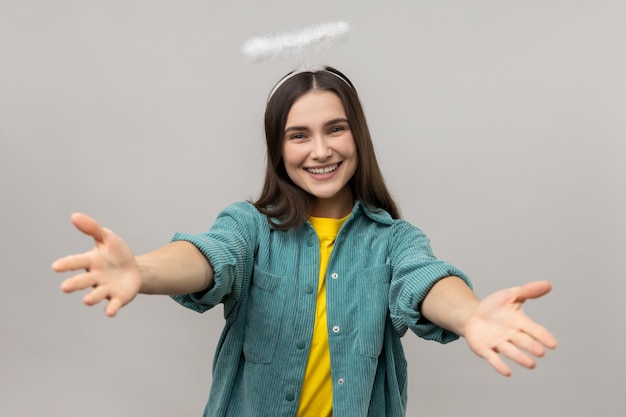 Attractive angelic woman with halo over head stretching arms to camera with kind friendly smile