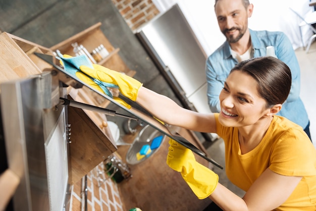 Attractive appealing charming wife holding cover while polishing it and laughing