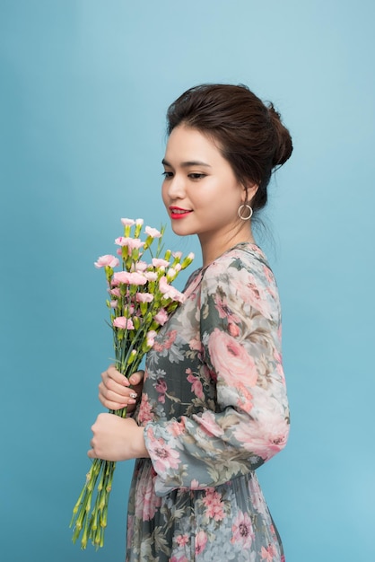 Attractive Asia woman in romantic dress holding bouquet of flowers over blue background