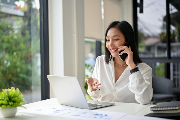 Attractive Asian businesswoman talking on the phone with her business partner dealing business