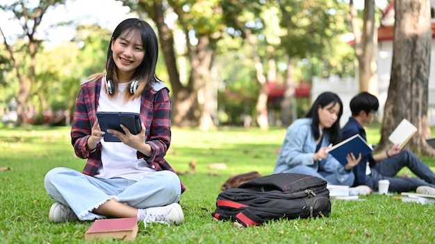 Attractive Asian female college student using her tablet while relaxes sitting in the campus's park