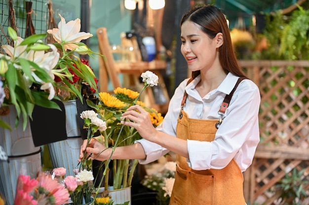 Attractive Asian female florist arranging flowers in a vase in her shop