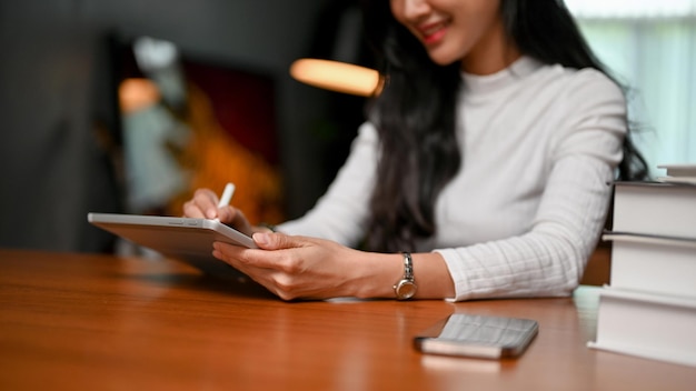 Attractive asian female freelancer using her tablet while sitting at her home working table