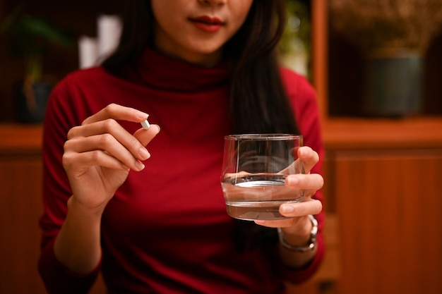 Attractive Asian female holding a glass of water and a tablet medicine cropped image