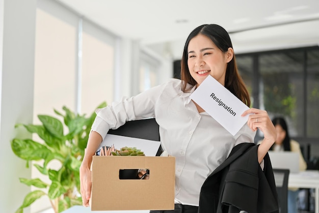 Attractive Asian female office worker happy to resign from her boring job carrying cardboard box