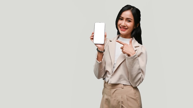 Attractive Asian female showing smartphone mockup standing isolated over grey background