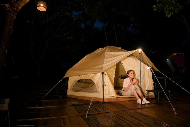 Attractive Asian female sitting in front of her camping tent looking at the night beautiful sky