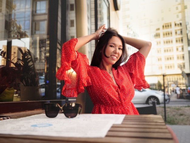 Attractive Asian girl in a red dress pin up her hair on the summer terrace of a cafe.