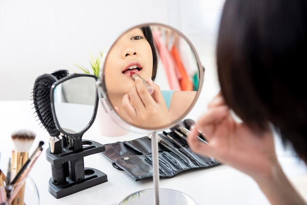 Attractive asian woman applying red lipstick in front of mirror