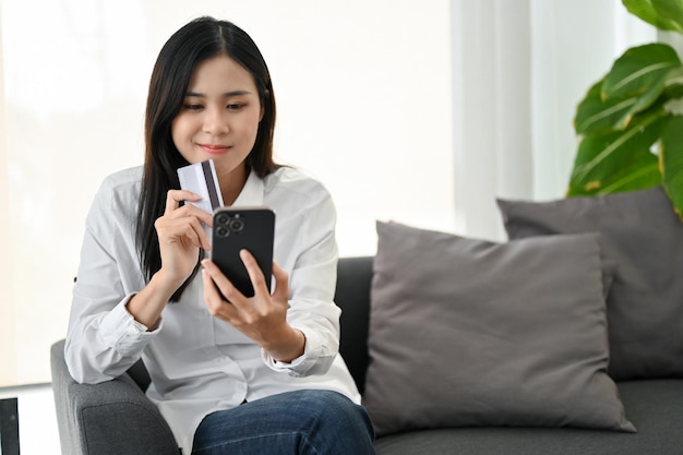 Attractive Asian woman holding a smartphone and a credit card enjoys shopping online