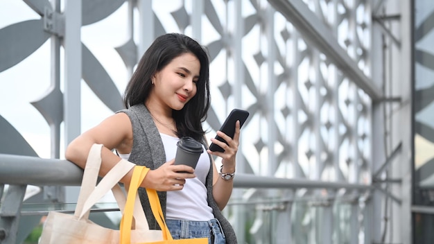 Attractive asian woman standing on terrace of shopping mall and using mobile phone