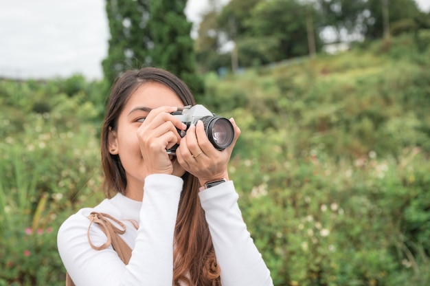 Attractive asian woman taking photo with retro film camera among the nature at countryside in the morning