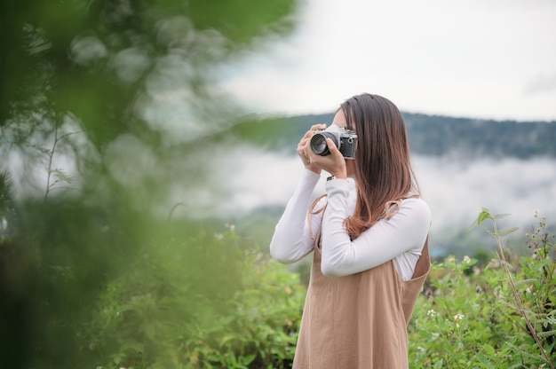 Attractive asian woman taking photo with retro film camera among the nature at countryside in the morning