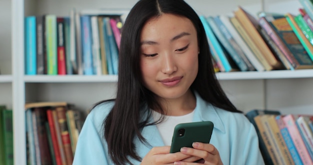 Attractive asian woman took a break between studies and using smartphone texting message while standing in the library University library concept