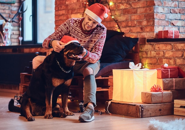 Photo attractive bearded hipster male with his rottweiler dog in a room with christmas decoration.