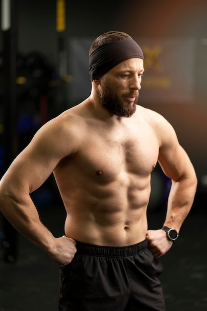 Attractive bearded man athlete with naked pumped up torso training in gym standing looking away